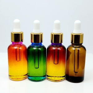 May include: Four glass bottles with gold caps and white droppers. The bottles are filled with a clear liquid and have a gradient color effect. The colors are orange, green, yellow, and brown.
