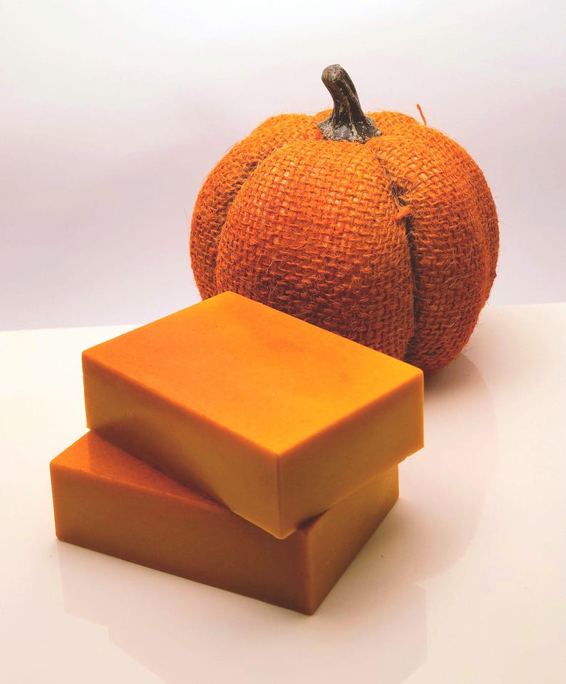 May include: Two orange bars of soap stacked on top of each other. The soap is in the shape of a rectangle. A burlap pumpkin is in the background.