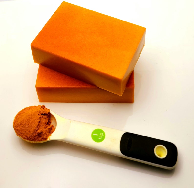 May include: Two orange bars of soap stacked on top of each other. A white measuring spoon with a green label that says "1 tsp" is filled with orange powder.