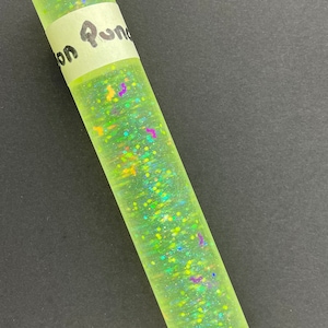 May include: A yellow, translucent tube filled with iridescent glitter. The tube has a white label with the text "on Pun" written on it.