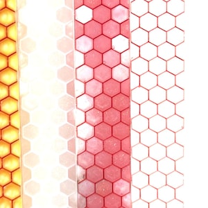 May include: Four vertical strips featuring a repeating hexagonal honeycomb pattern. The first strip is yellow, the second is a translucent white, the third is a glittery pink, and the fourth is a white strip with a thin red hexagonal grid outline.