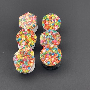 May include: Six colourful phone grips with a fruit and candy design. The grips are round and have a white base.
