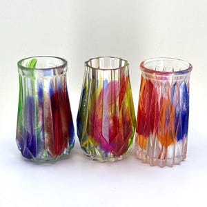 May include: Three clear glass candle holders with colourful feather designs. The candle holders are different shapes and sizes.
