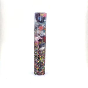 May include: A cylindrical resin object featuring a clear upper section filled with tangled multicolored threads and a dense lower section packed with small, square, multicolored glitter pieces. The item has a smooth, glossy finish throughout its length.