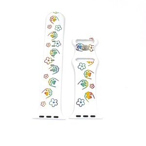 May include: White watch band with a repeating pattern of rainbow-colored paw prints and flowers. The band is made of a flexible material and has a buckle closure. The watch band is designed to fit a smartwatch.
