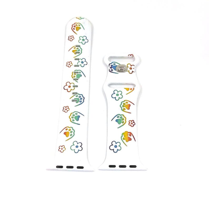 May include: White watch band with a repeating pattern of rainbow-colored paw prints and flowers. The band is made of a flexible material and has a buckle closure. The watch band is designed to fit a smartwatch.