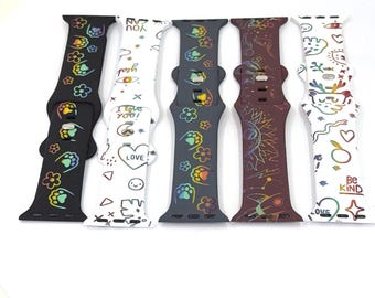 May include: Six colorful watch bands with various designs. The bands include black, white, gray, and maroon colors. Each band features unique patterns, including flowers, paw prints, and inspirational phrases like "I love you!" and "Be Kind."
