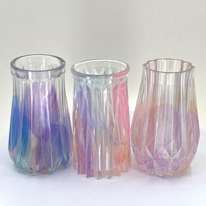 May include: Three iridescent glass vases with a geometric pattern. The vases are clear with a rainbow of colours, including pink, blue, and purple.