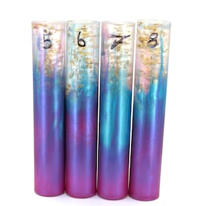 May include: Four cylindrical resin objects with a gradient of purple to teal and gold leaf accents. Each cylinder is numbered with a black marker, from 5 to 8. The objects are standing upright against a white background.