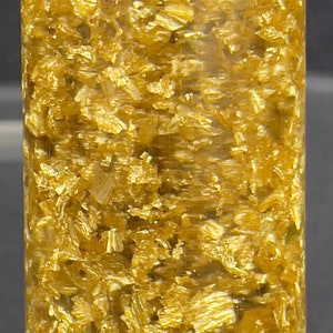 May include: A clear glass tube filled with small, shiny, gold-colored flakes.