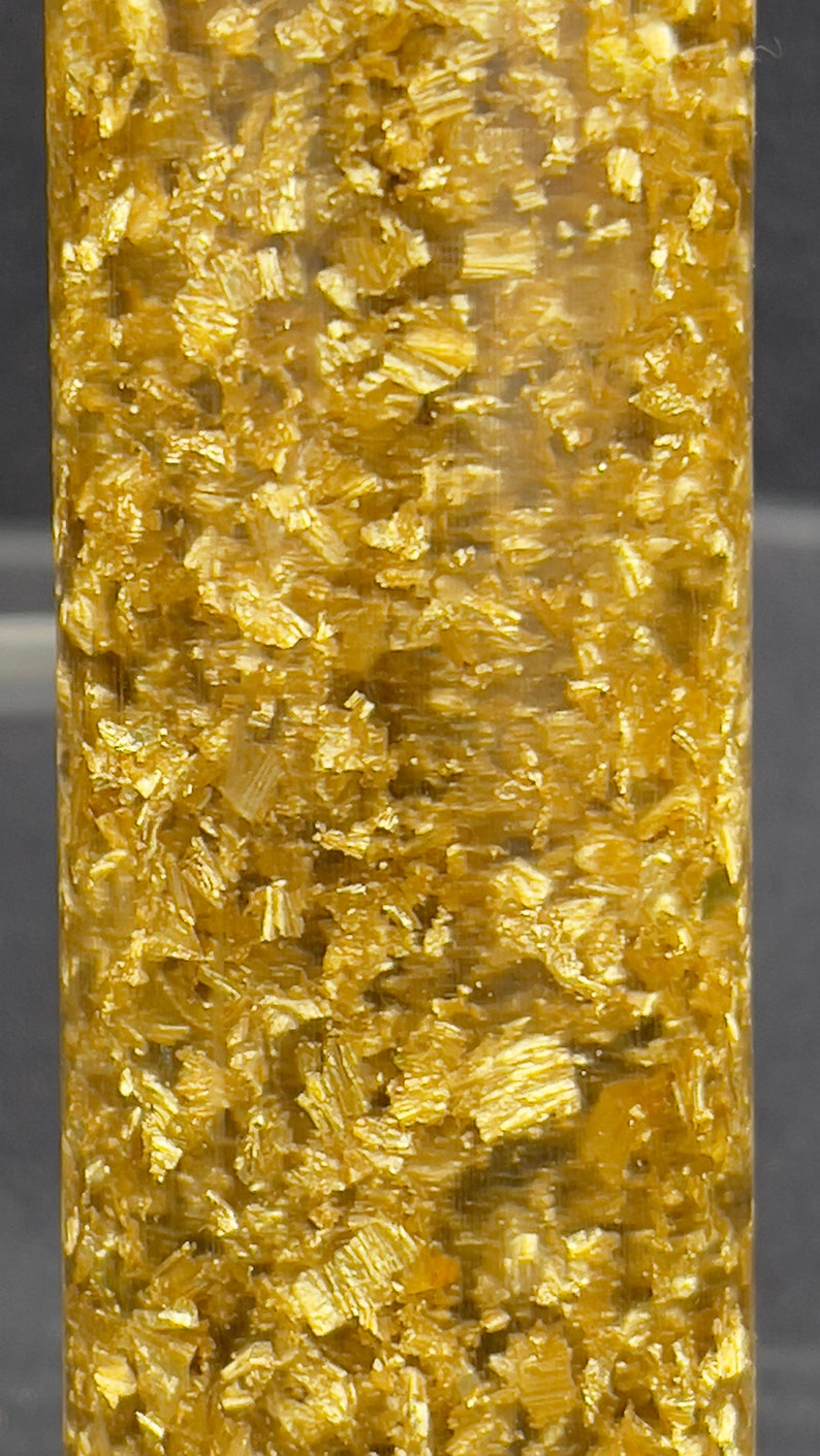 May include: A clear glass tube filled with small, shiny, gold-colored flakes.