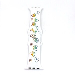 May include: White watch band with a repeating pattern of rainbow-colored paw prints and flowers. The band is made of a flexible material and has a clasp for securing it to a watch. The design is playful and colorful.