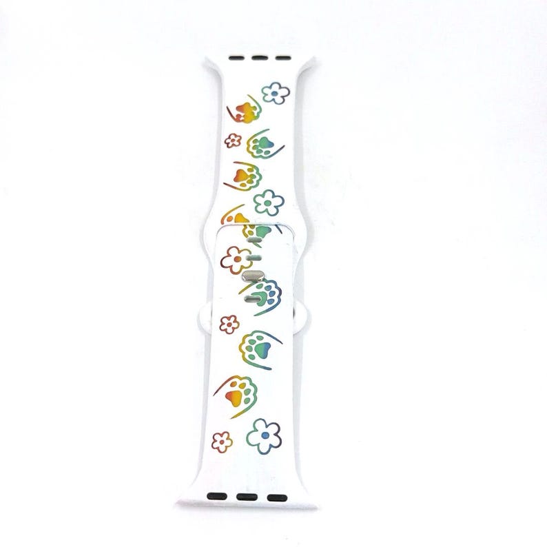 May include: White watch band with a repeating pattern of rainbow-colored paw prints and flowers. The band is made of a flexible material and has a clasp for securing it to a watch. The design is playful and colorful.