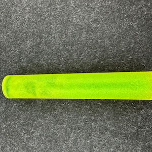 May include: A neon green, cylindrical object with rounded ends. The object has a slightly textured surface and appears to be made of a translucent material. It is set against a dark gray, textured background.