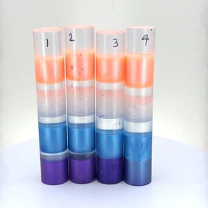 May include: Four cylindrical resin blanks arranged vertically, each featuring horizontal color bands of orange, white, blue, and purple. The cylinders are numbered 1 through 4 at the top. Each blank displays a unique gradient and glitter texture.