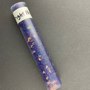 May include: A clear tube filled with a dark blue and purple glitter mixture with gold flecks. The tube has a white label that says "Right Now".