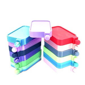 May include: Stacks of colorful, rectangular containers in shades of blue, purple, green, and red. Each container has a small, round knob on the side. The containers are stacked on top of each other.