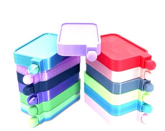May include: Stacks of colorful, rectangular containers in shades of blue, purple, green, and red. Each container has a small, round knob on the side. The containers are stacked on top of each other.