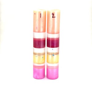 May include: Two cylindrical resin pen blanks standing upright, each featuring horizontal stripes of peach, white, deep magenta, translucent white, yellow, and pink. The left blank is marked with the number 1 and the right with the number 2 in black ink.