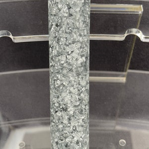 May include: A clear cylinder filled with silver glitter. The glitter is evenly distributed throughout the cylinder.