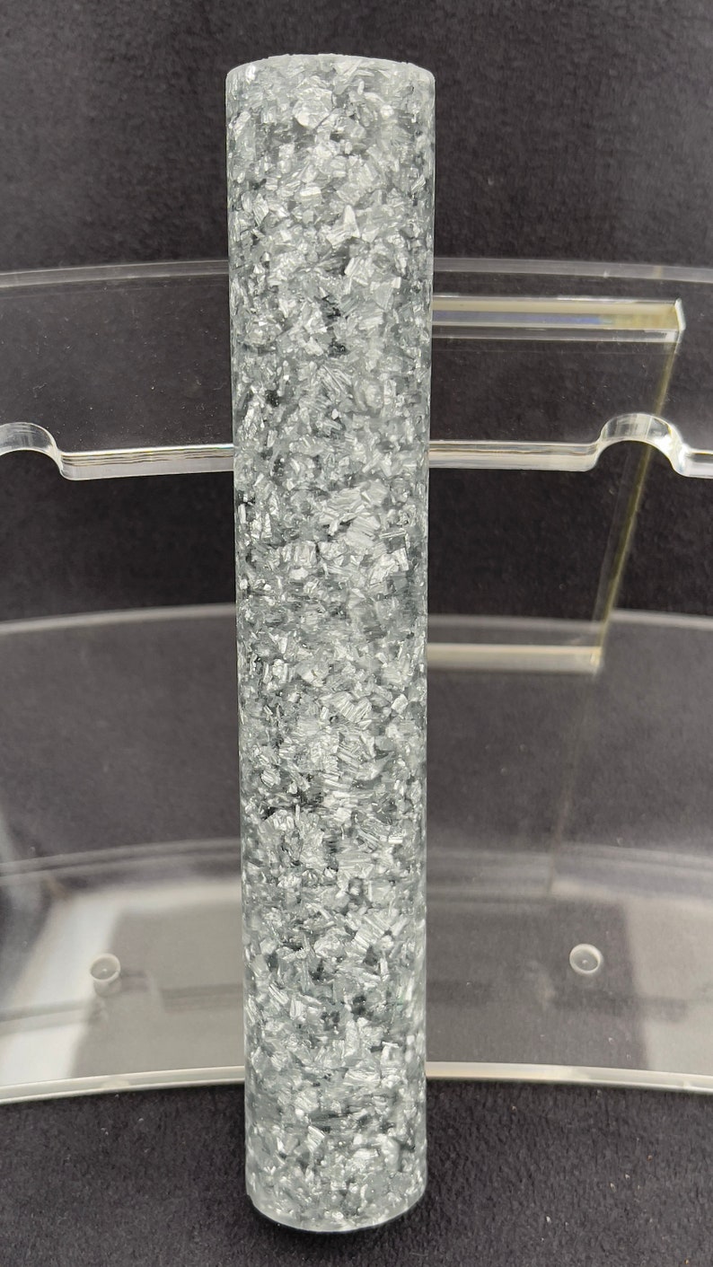 May include: A clear cylinder filled with silver glitter. The glitter is evenly distributed throughout the cylinder.
