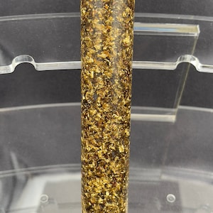 May include: A long, cylindrical, dark brown and gold pen blank with gold flecks throughout.