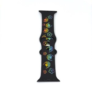 May include: Black watch band with a repeating pattern of colorful paw prints and flowers. The band is made of a flexible material and has a buckle closure. The paw prints and flowers are in a rainbow of colors.