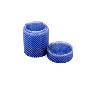 May include: A blue, open, cylindrical container with a textured, swirling pattern. The container is made of a translucent material and has a lid.