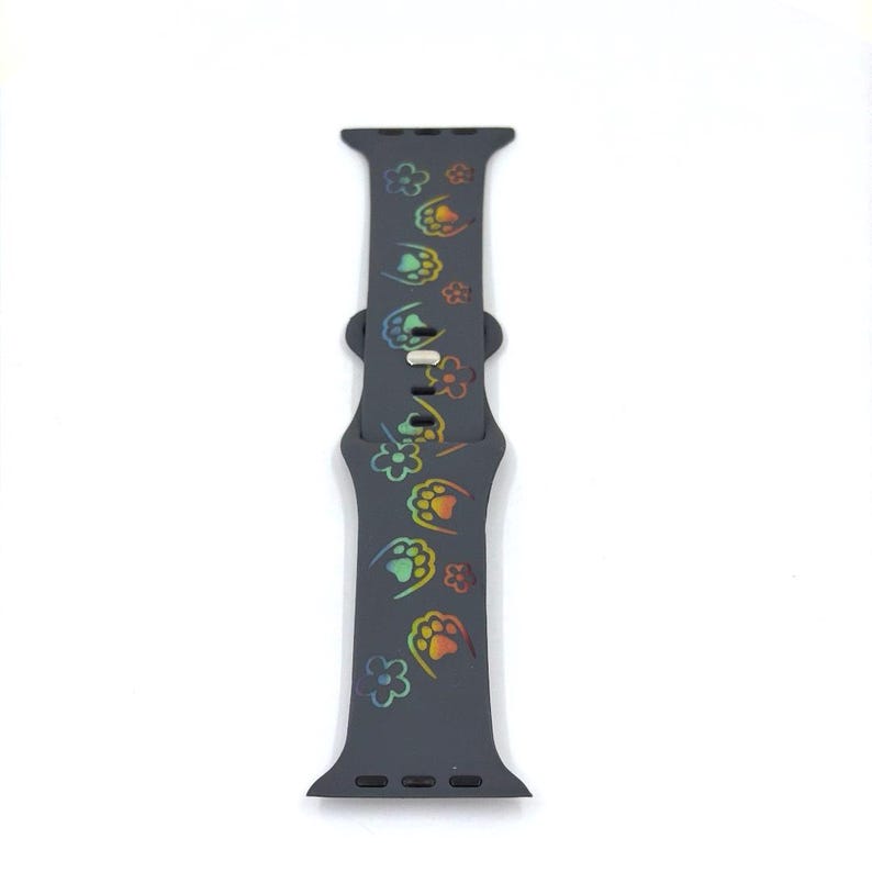 May include: A dark gray watch band with a repeating pattern of colorful paw prints. The paw prints are in shades of red, orange, yellow, green, and blue. The band is made of a flexible material and has a buckle closure.
