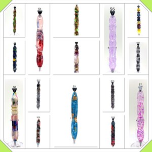 May include: A collection of 15 colorful pens with unique designs. Each pen has a different pattern and color combination, including blue, green, red, purple, and black. The pens are arranged in a grid pattern on a white background.