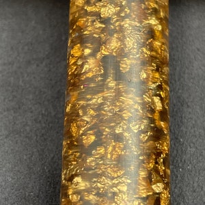 May include: A close-up of a gold and brown pen with a textured surface. The pen is covered in gold flakes.