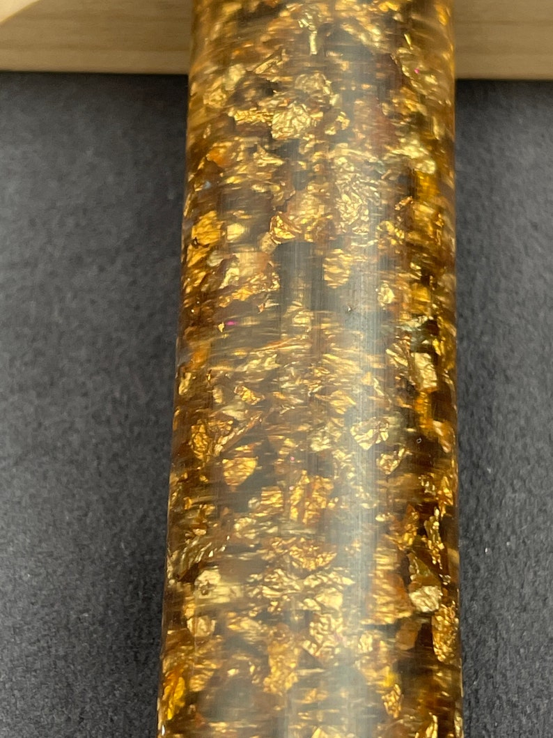 May include: A close-up of a gold and brown pen with a textured surface. The pen is covered in gold flakes.