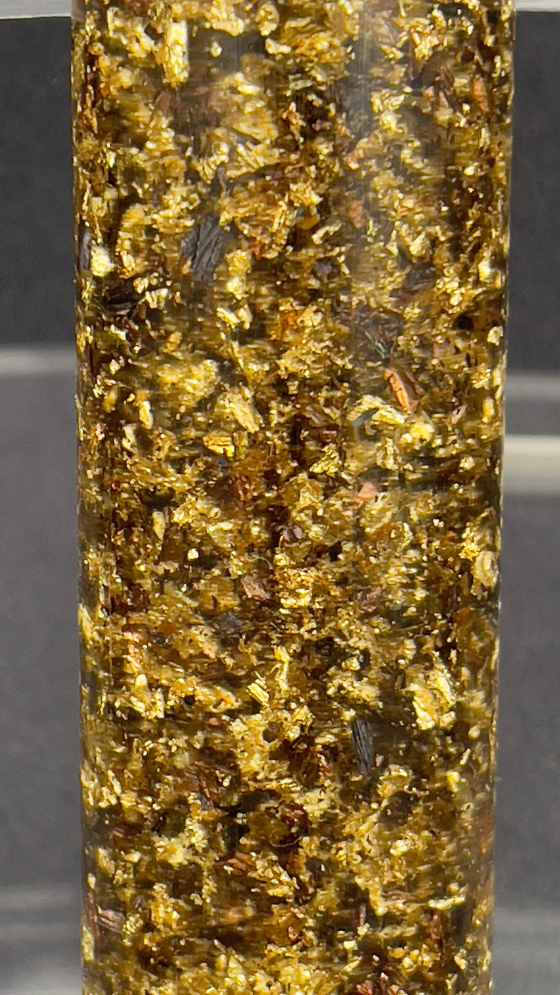 May include: A close-up of a cylindrical sample of a dark green material with flecks of gold throughout.