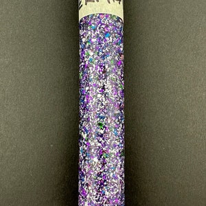 May include: A clear tube filled with purple, blue, green, and silver glitter. The tube has a white label with the word "ERMA" written in black marker.