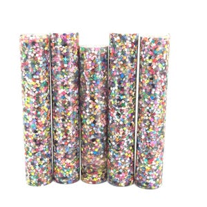 May include: Five cylindrical objects arranged in a row, each featuring a dense, multi-colored mosaic pattern of tiny square-shaped pieces in shades of pink, blue, yellow, green, and white, creating a vibrant, textured appearance across the surfaces.
