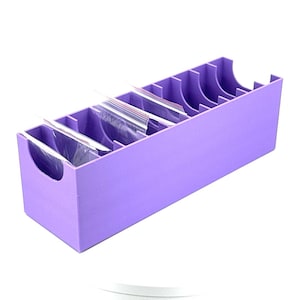 May include: A lavender organiser with multiple compartments, each designed to hold small, clear plastic bags. The rectangular container has a handle cutout on one end and curved cutouts on the top edge of each compartment.