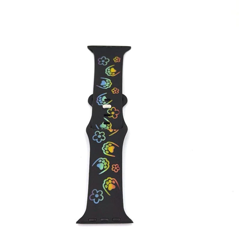 May include: Black smartwatch band with a repeating pattern of paw prints and flowers in a rainbow gradient. The band is made of a flexible material and has a buckle closure. The band is designed to fit a smartwatch.
