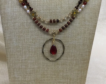 Double-strand pendant length necklace with hammered brass ring and ruby colored drop.