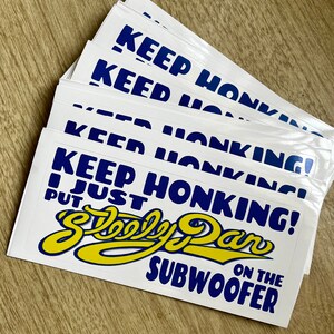 May include: A stack of white stickers with blue text that reads "Keep Honking! I Just Put a  Steely Dan on the Subwoofer". The text is in a bold, stylized font. The stickers are printed on white paper and have a glossy finish.