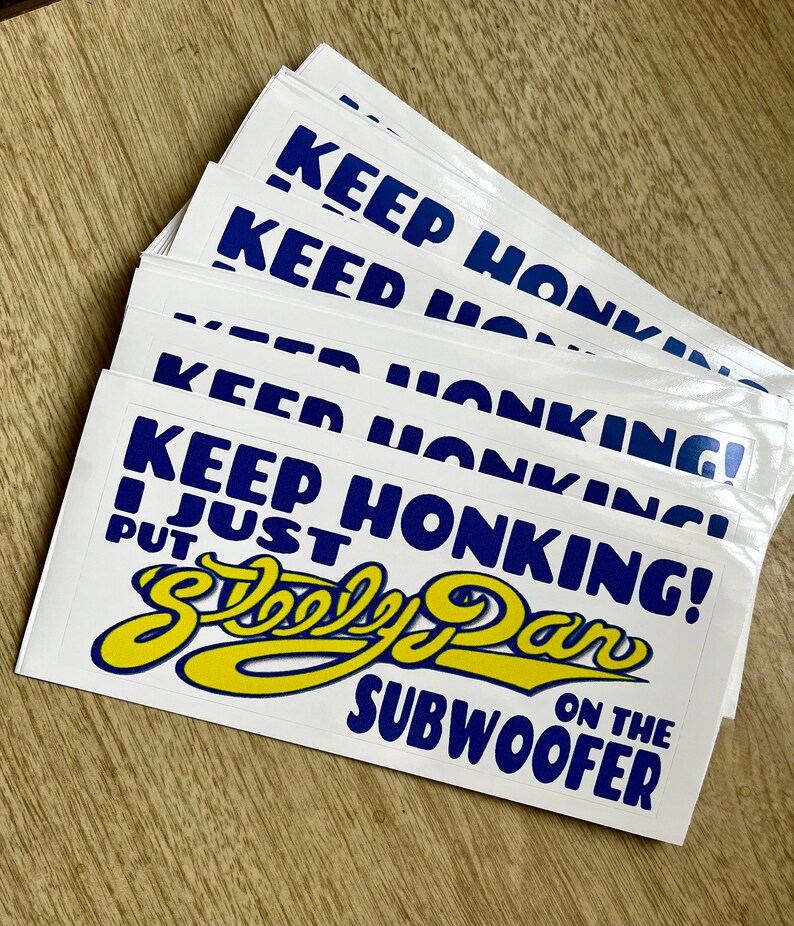 May include: A stack of white stickers with blue text that reads "Keep Honking! I Just Put a  Steely Dan on the Subwoofer". The text is in a bold, stylized font. The stickers are printed on white paper and have a glossy finish.