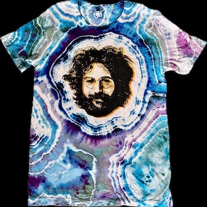 Könnte beinhalten: Ein Batik-T-Shirt mit einem psychedelischen Wirbelmuster in Blautönen, Lila und Weiß. Das Shirt zeigt im Zentrum ein Schwarzweißbild von Jerry Garcia.