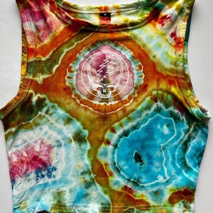 May include: A tie-dye crop top in vibrant colors of orange, blue, pink, and green. The top features a white graphic of a skull with a lightning bolt on the front. The sleeveless top has a round neckline.