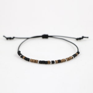 Peut inclure: Un bracelet en cordon noir avec des perles carr&eacute;es brunes et argent&eacute;es.