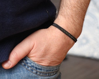 Può includere: Un braccialetto nero con perline e dettagli dorati. Il braccialetto è indossato al polso.