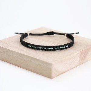 Könnte beinhalten: Ein schwarzes und grünes Perlenarmband mit einem verschiebbaren Knotenverschluss.