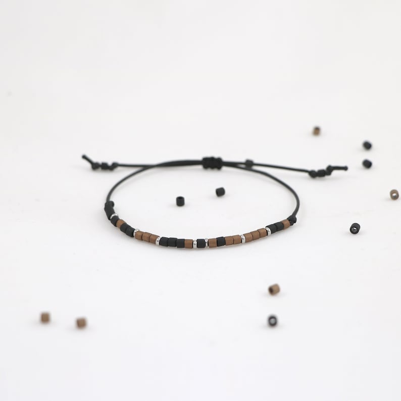Peut inclure: Un bracelet en cordon noir avec des perles brunes et noires. Le bracelet est r&eacute;glable et poss&egrave;de un n&oelig;ud coulissant.