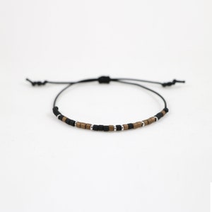 Peut inclure: Un bracelet en cordon noir avec des perles carr&eacute;es brunes et argent&eacute;es.