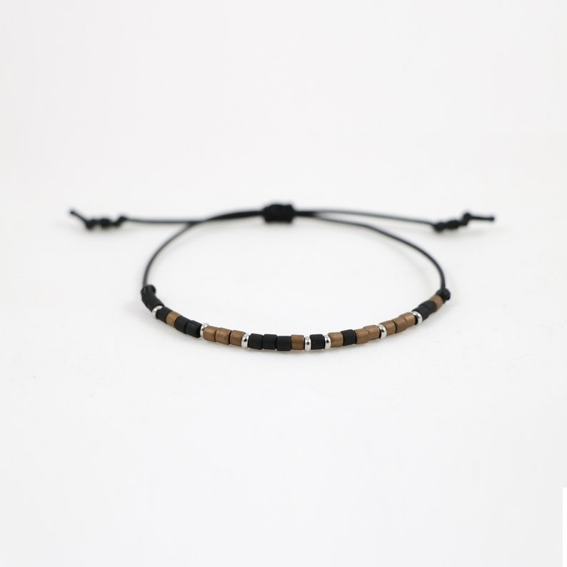 Peut inclure: Un bracelet en cordon noir avec des perles carr&eacute;es brunes et argent&eacute;es.