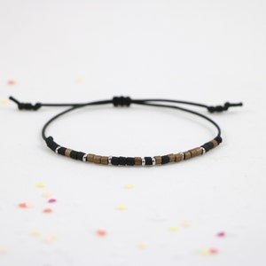 Peut inclure: Un bracelet en cordon noir avec des perles carr&eacute;es dor&eacute;es et argent&eacute;es.