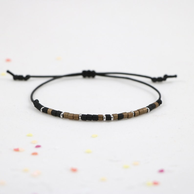 Peut inclure: Un bracelet en cordon noir avec des perles carr&eacute;es dor&eacute;es et argent&eacute;es.